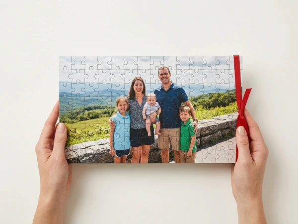 Hands holding a finished photo puzzle of a family with a baby on a hilltop