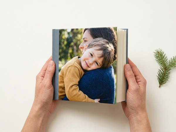 Hands holding open a photo book with a boy hugging his mom on the cover