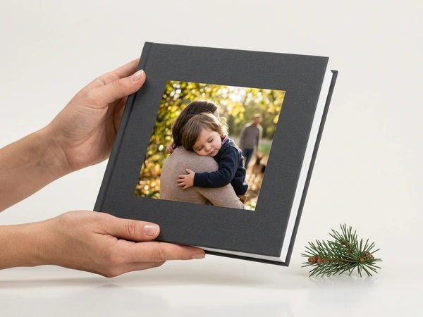 Hands holding a finished gray photo book with a cover window photo of a hug