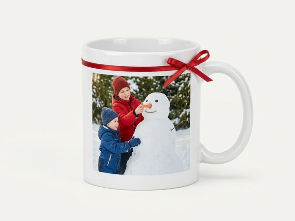 White photo mug tied with red ribbon of two children building a snowman