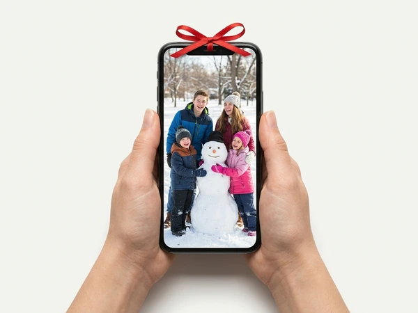 Hands holding a phone with a red bow showing a family with a snowman