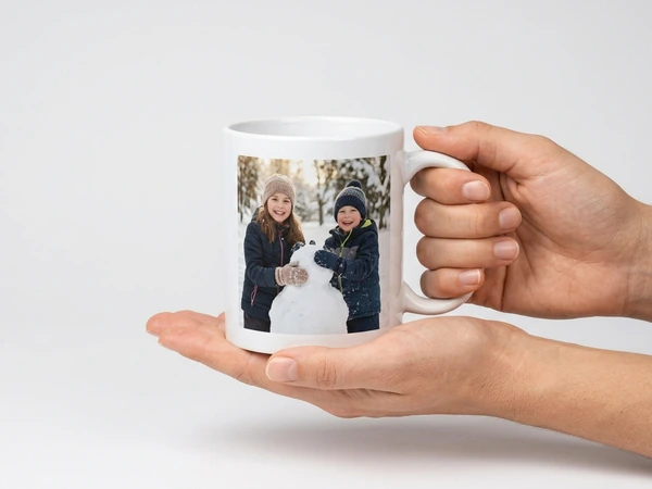Hand holding a photo mug of two children with a snowman