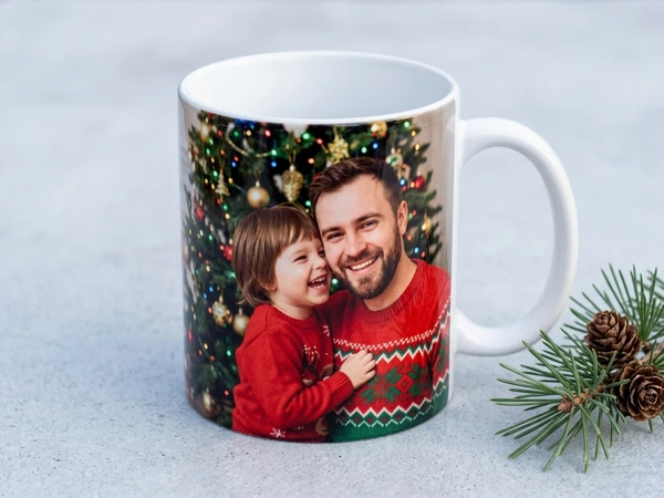 White photo mug of a man and a small boy in red sweaters laughing by a Christmas tree