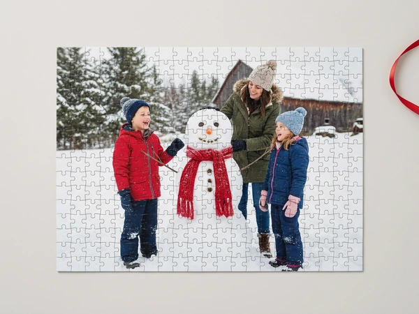 Photo puzzle of a woman and two children in winter coats building a snowman by a barn