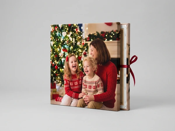 Square canvas of a woman and two laughing children in red knit sweaters by a lit Christmas tree