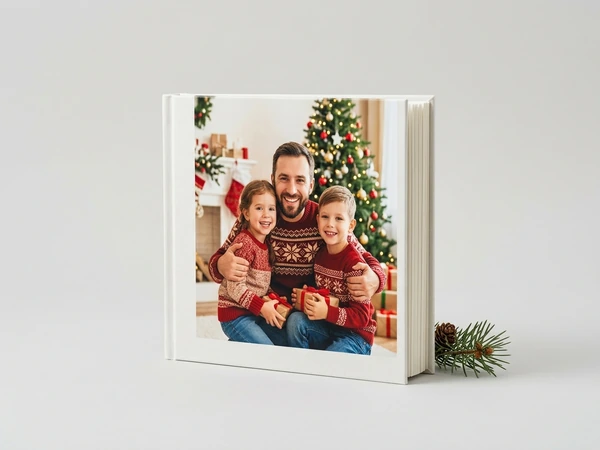 White hardcover photo book of a man hugging two children in holiday sweaters by a Christmas tree