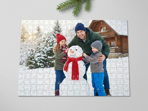 Photo puzzle of a man, a girl and a boy building a snowman in front of a snowy log cabin
