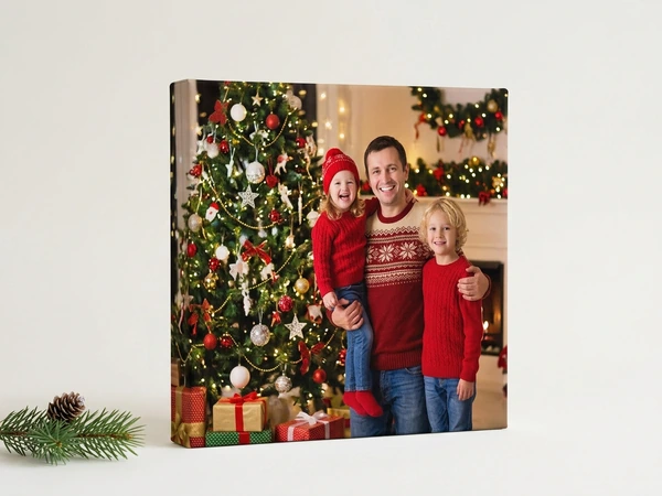 Square canvas of a man holding a girl in a red hat beside a boy by a decorated Christmas tree