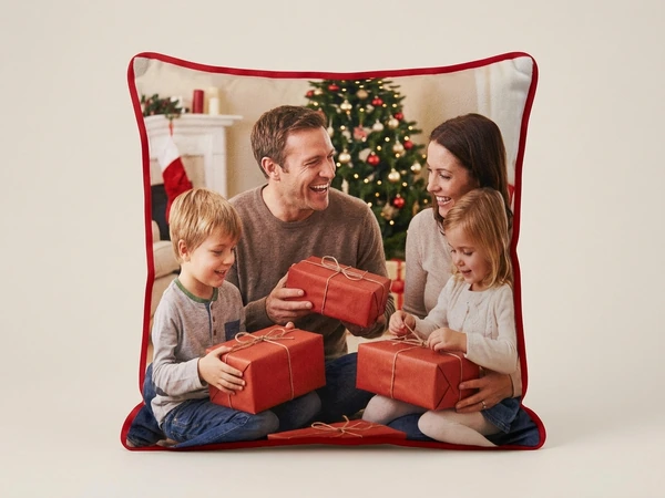 Plush pillow with red piping of a family of four opening red wrapped gifts