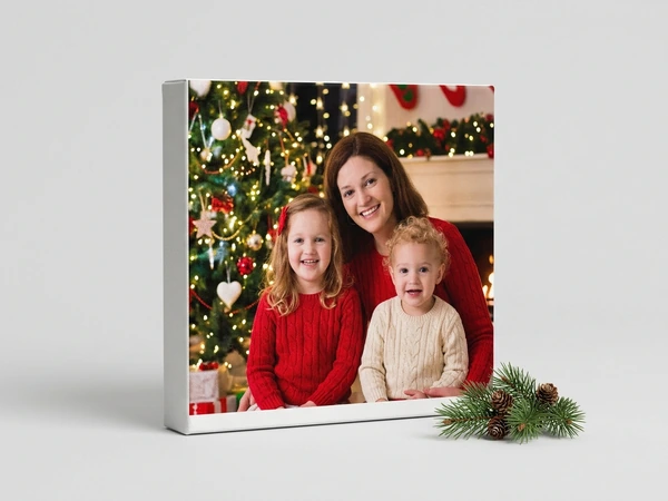 Square canvas with a white edge of a woman, a girl and a toddler in red sweaters by a Christmas tree