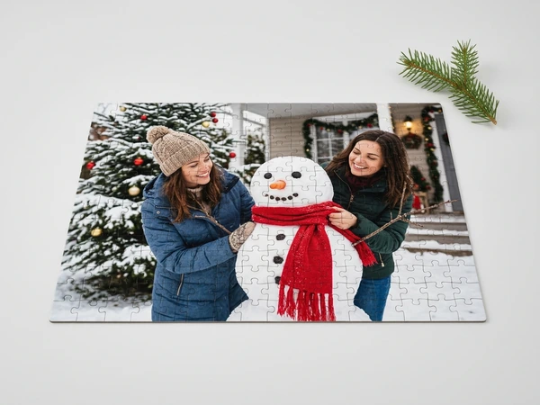 Photo puzzle of two women building a snowman with a red scarf outside a house