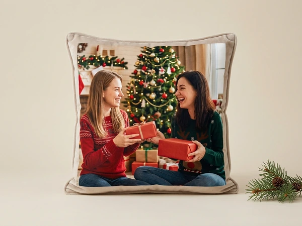 Plush pillow of two women exchanging red gifts beside a Christmas tree