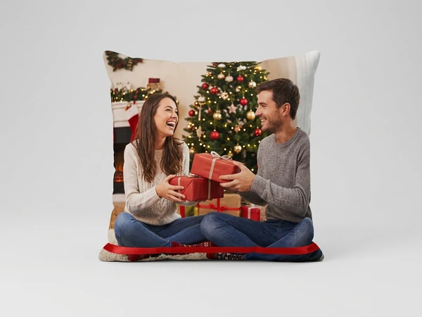 Plush pillow of a man and a woman exchanging red gifts in front of a Christmas tree