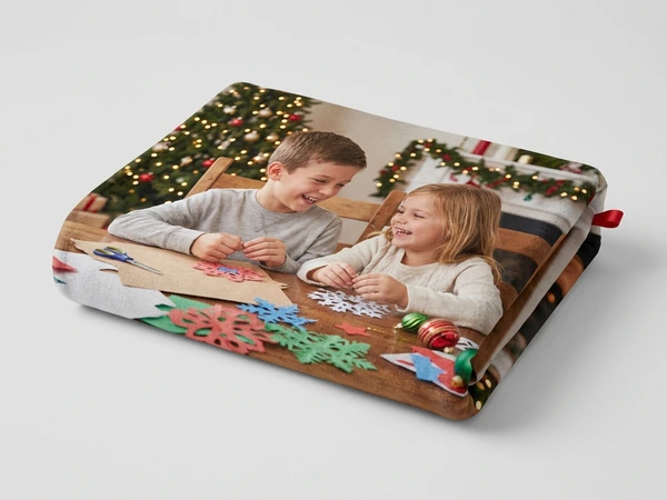 Folded fleece blanket of a boy and a girl cutting paper snowflakes at a wooden table