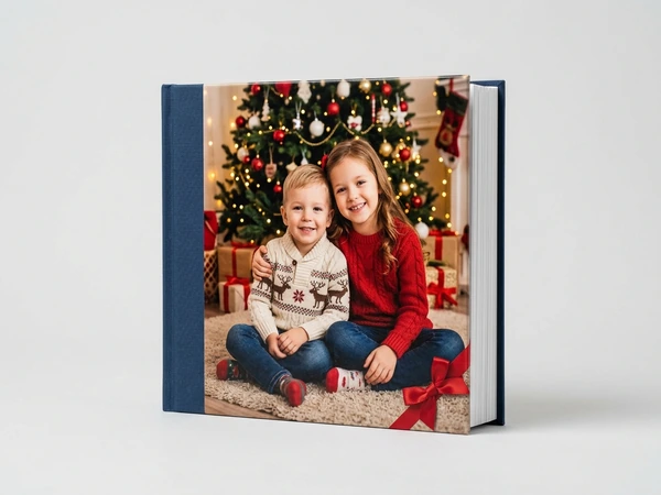 Photo book with a navy spine of a boy and a girl sitting on a rug by a Christmas tree
