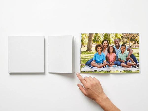Hand pointing to one of three photo books, two with plain white covers and one open on a family picnic photo