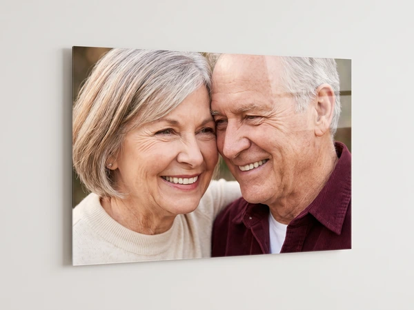 Acrylic print shown at an angle, an older couple smiling cheek to cheek, its clear edge catching the light