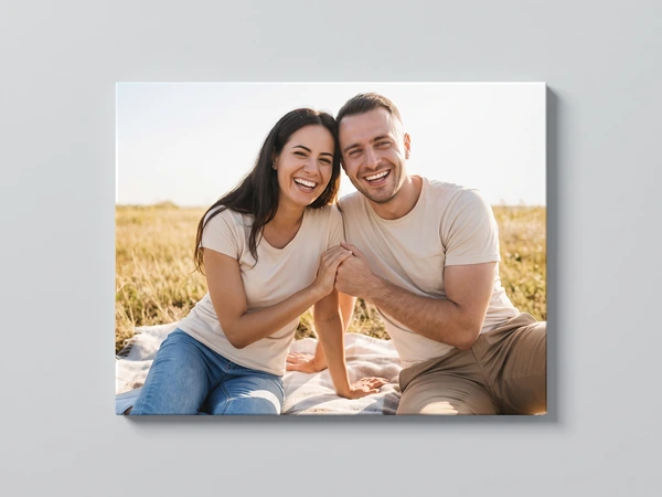 Canvas print of a laughing couple sitting on a blanket in a summer field