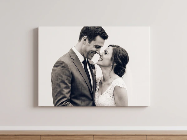 Black and white canvas print of a groom and bride touching foreheads, hung above a wooden sideboard