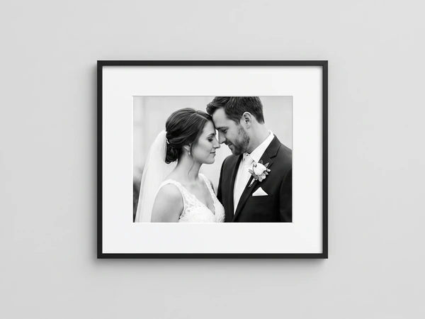Black framed black and white photo of a bride in a veil and a groom touching foreheads