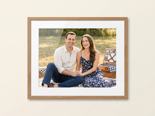 Oak framed print of a young couple sitting on a picnic blanket in the sun