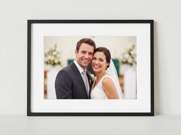 Black framed print of a bride and groom smiling cheek to cheek in a white hall