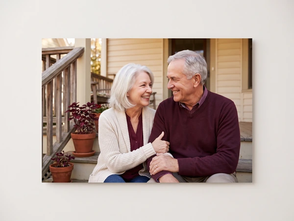 Metal print of an older couple sitting on the steps of a cream-colored house