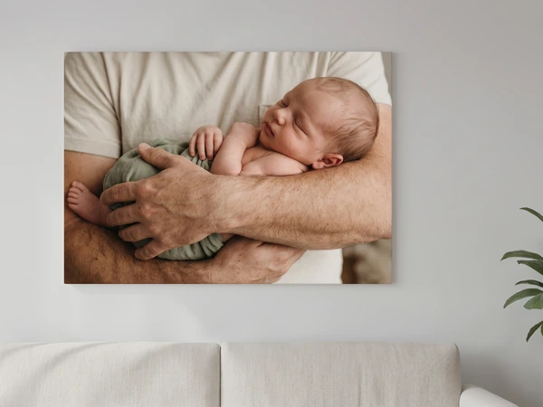 Acrylic print of a newborn sleeping in a man's arms, hung above a gray sofa