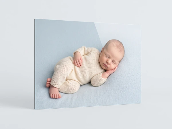 Acrylic print at an angle of a newborn in a cream knit suit asleep on a pale blue blanket