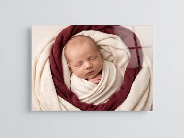 Acrylic print of a sleeping newborn swaddled in cream inside a burgundy wrap