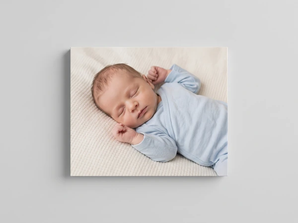 Canvas print of a newborn in a blue sleepsuit asleep on a cream blanket