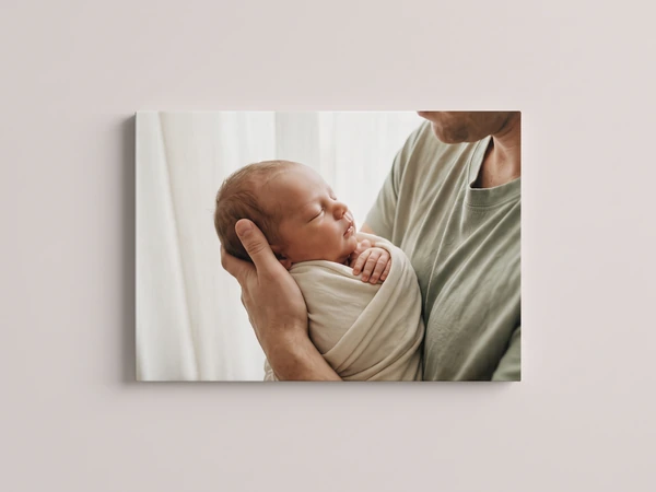 Canvas print of a parent's hands holding a swaddled sleeping newborn, the photo wrapping the edges