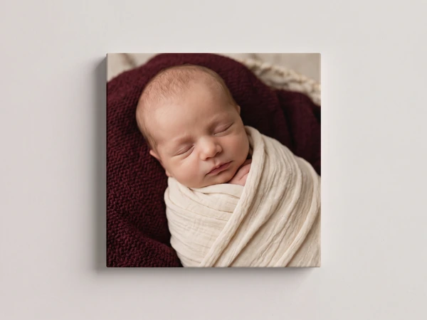 Canvas print of a sleeping newborn swaddled in cream on a burgundy blanket