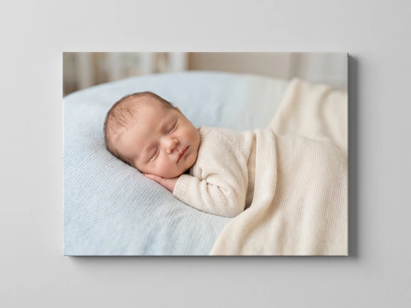 Canvas print of a newborn asleep on a pale blue cushion under a cream blanket