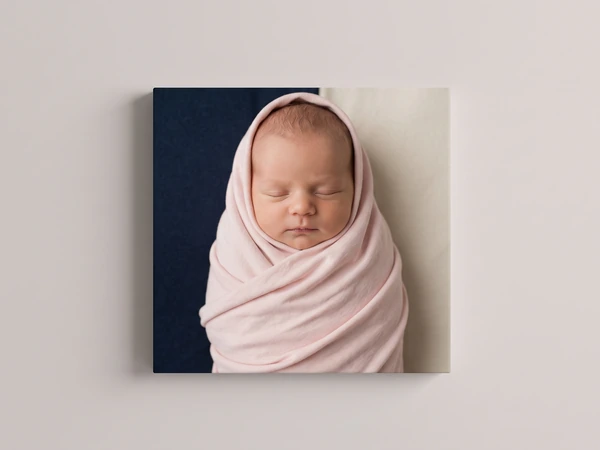 Portrait canvas print of a newborn swaddled in pink against a navy background