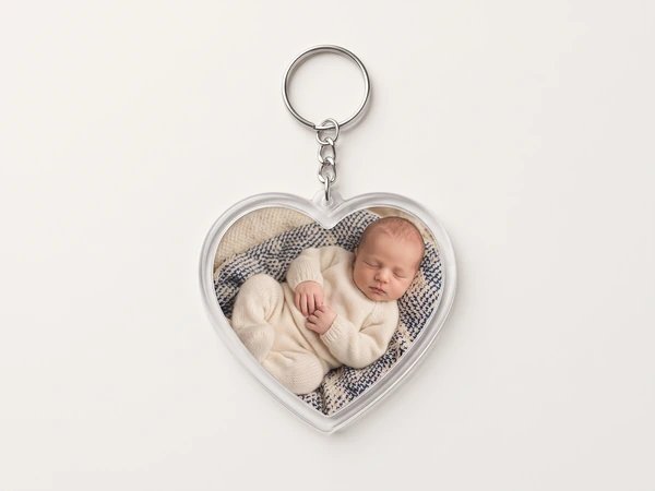Heart keychain on a chain with a photo of a baby in a cream knit suit asleep on a blanket