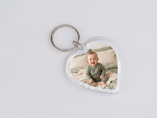 Heart keychain with a photo of a smiling baby in a green outfit sitting on a bed