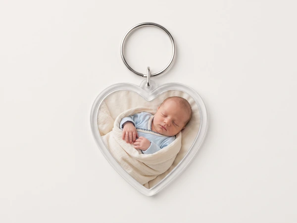Heart keychain with a photo of a newborn in a blue sleepsuit tucked in a cream blanket