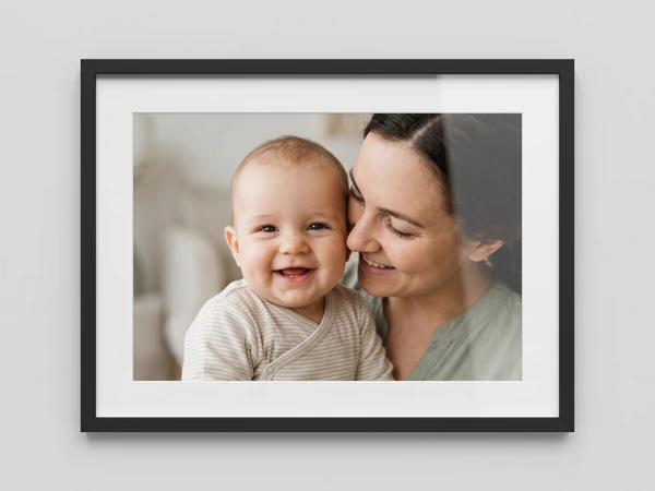 Black framed print of a laughing baby held cheek to cheek by its mother