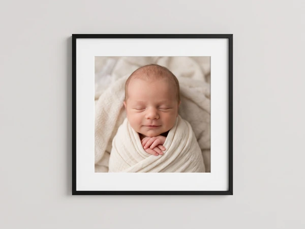 Black framed close-up print of a smiling newborn wrapped in cream