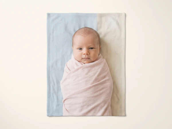 Blanket printed with a wide-eyed newborn swaddled in pink on a pale blue background