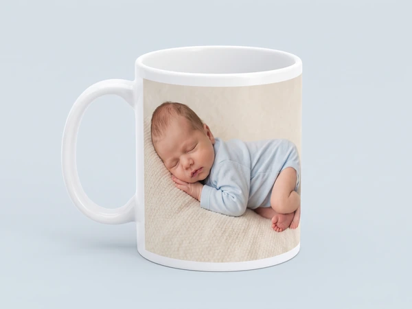 Photo mug on a pale blue background printed with a newborn asleep in a blue sleepsuit