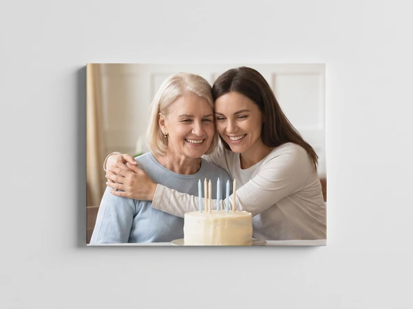 Canvas print of a mother and grown daughter hugging behind a birthday cake
