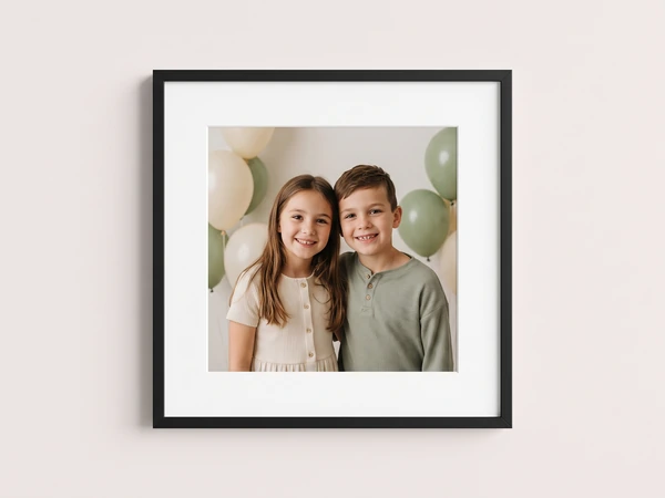Black framed print of a sister and brother smiling in front of sage balloons