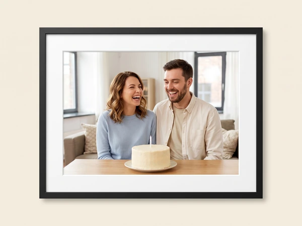 Black framed print of a laughing couple at a table with a white cake