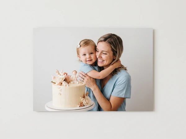 Metal print of a toddler hugging her mother beside a flower-topped cake