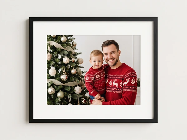 Black framed print of a father and toddler in matching reindeer sweaters by a tree