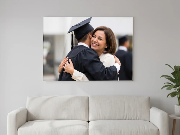 Acrylic print of a graduate in a black gown hugging his mother, hung above a white sofa