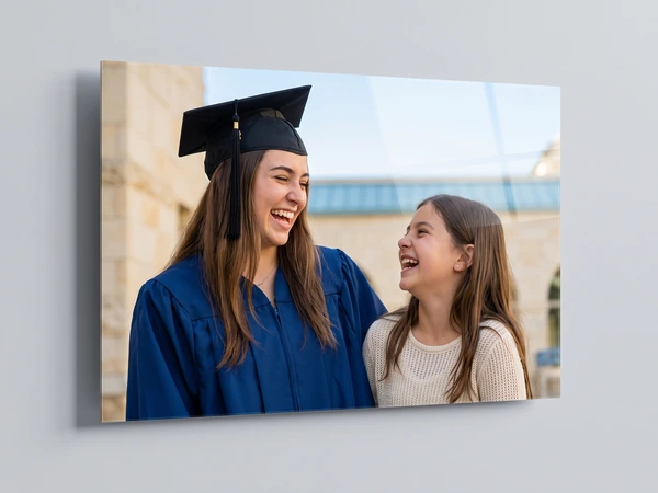 Acrylic print at an angle of a graduate in a navy gown laughing with her younger sister