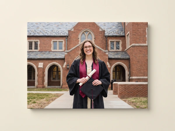 Canvas print of a graduate with a maroon stole holding her diploma outside a brick hall